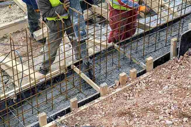Construction workers pouring reinforced concrete for a building foundation using steel rebar.