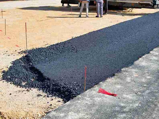 Finished residential driveway made of fresh asphalt with defined edges, surrounded by a light-colored surface.