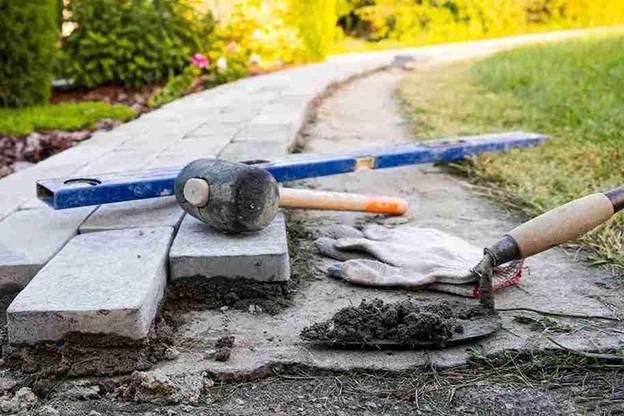 Tools and paving stones laid out for a concrete patio construction project in a residential backyard.