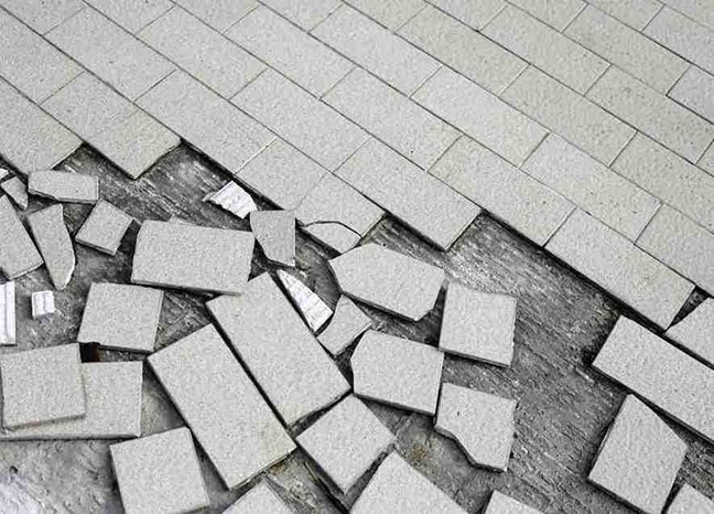 Broken and uneven concrete patio with damaged surface tiles showing cracks and missing sections.