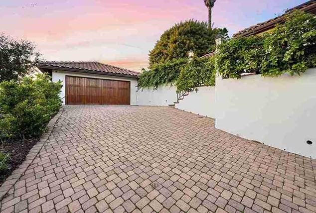 Beautiful paved patio with interlocking stone tiles leading to a garage, surrounded by greenery and white walls.