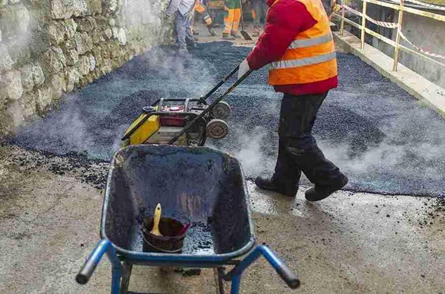 Worker operating a compactor to smooth and level freshly laid asphalt during driveway installation on a construction site.