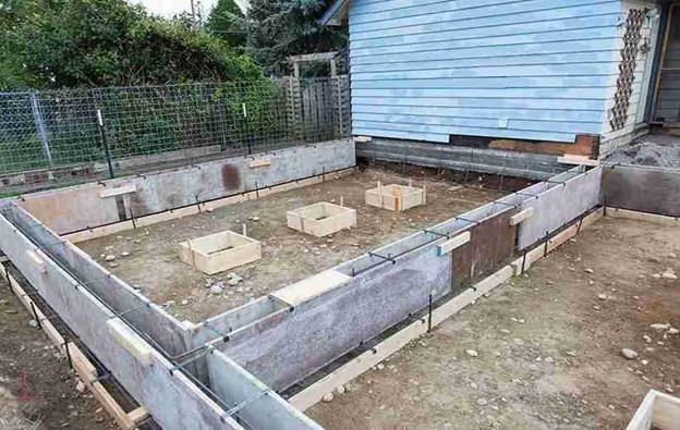 Residential concrete foundation under construction with formwork, rebar, and wooden framing in place.
