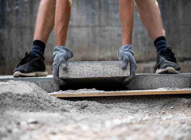 Two workers placing a large concrete slab on gravel foundation during installation.