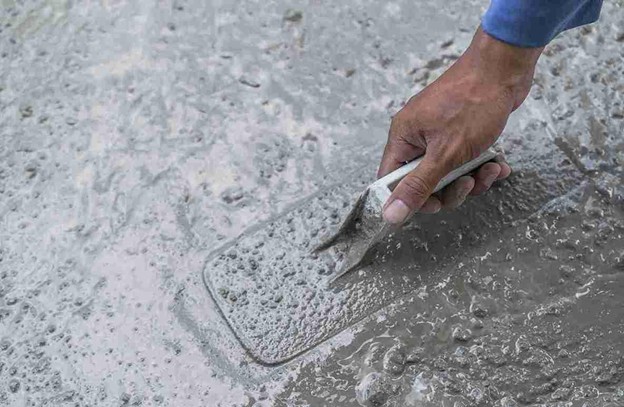 Hand smoothing wet concrete with a trowel to resurface and level a driveway or walkway.